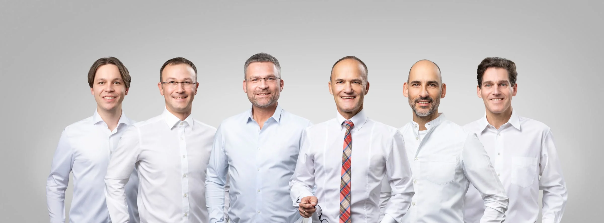 Die sechs Fachärzte des Orthopädischen Zentrums Darmstadt in weißen Hemden vor grauem Studiohintergrund